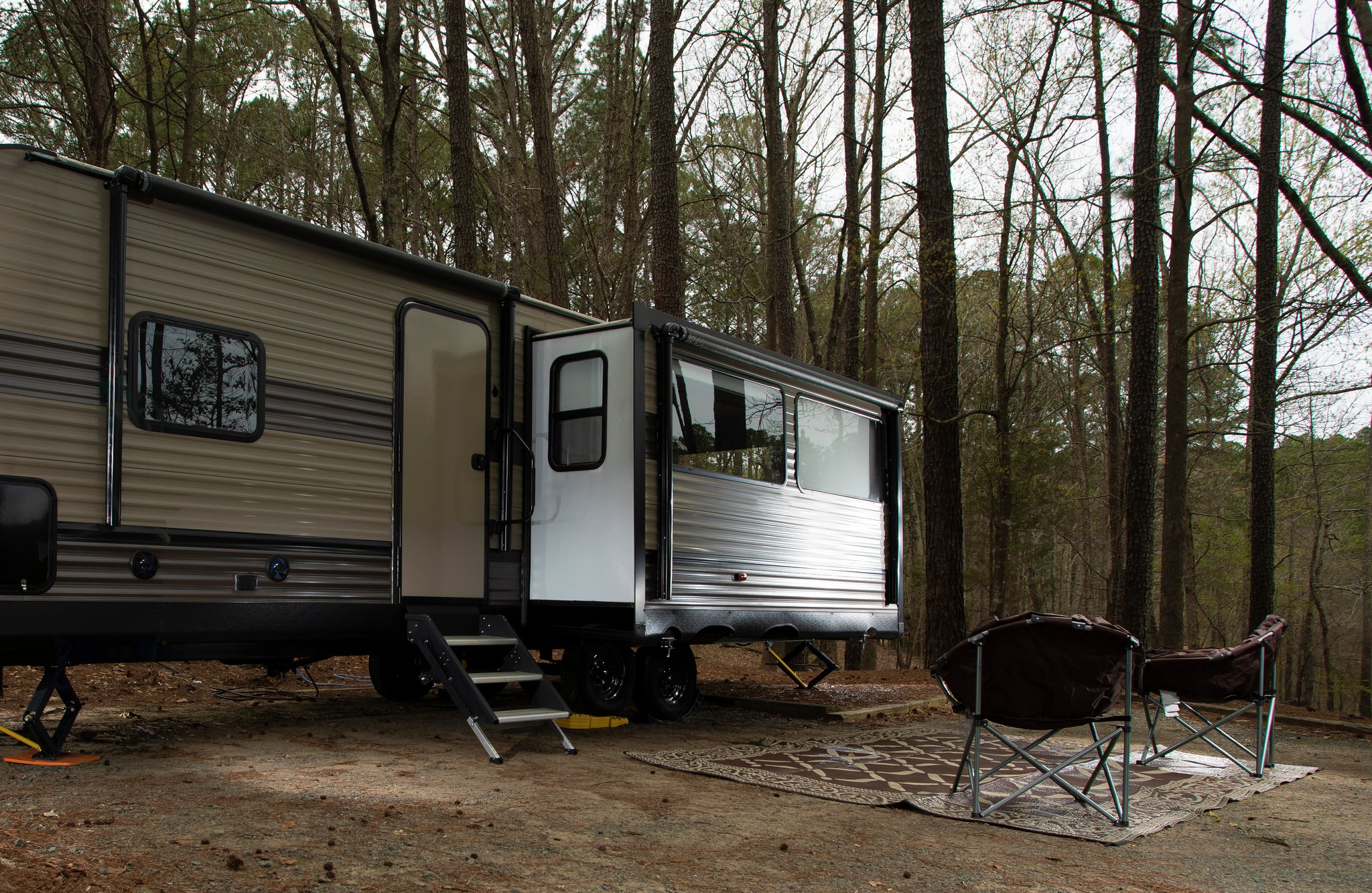 A parked RV with its slide-out fully extended. There are a couple of chairs sitting outside facing it.