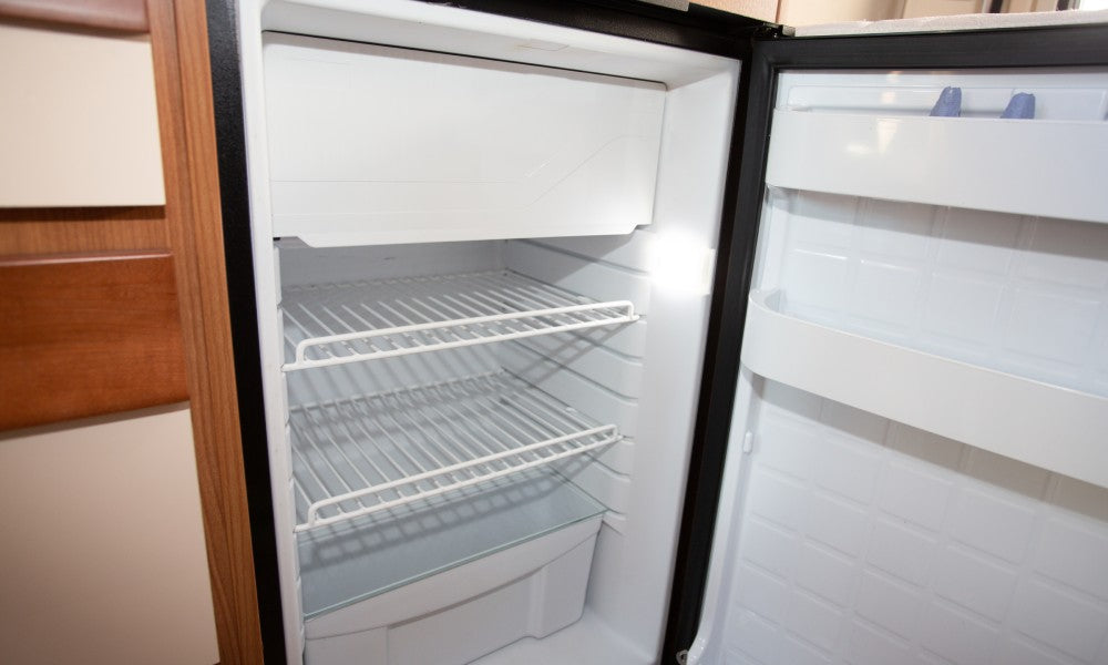 An RV fridge with the door open. There isn't anything inside of the fridge and it looks quite clean.