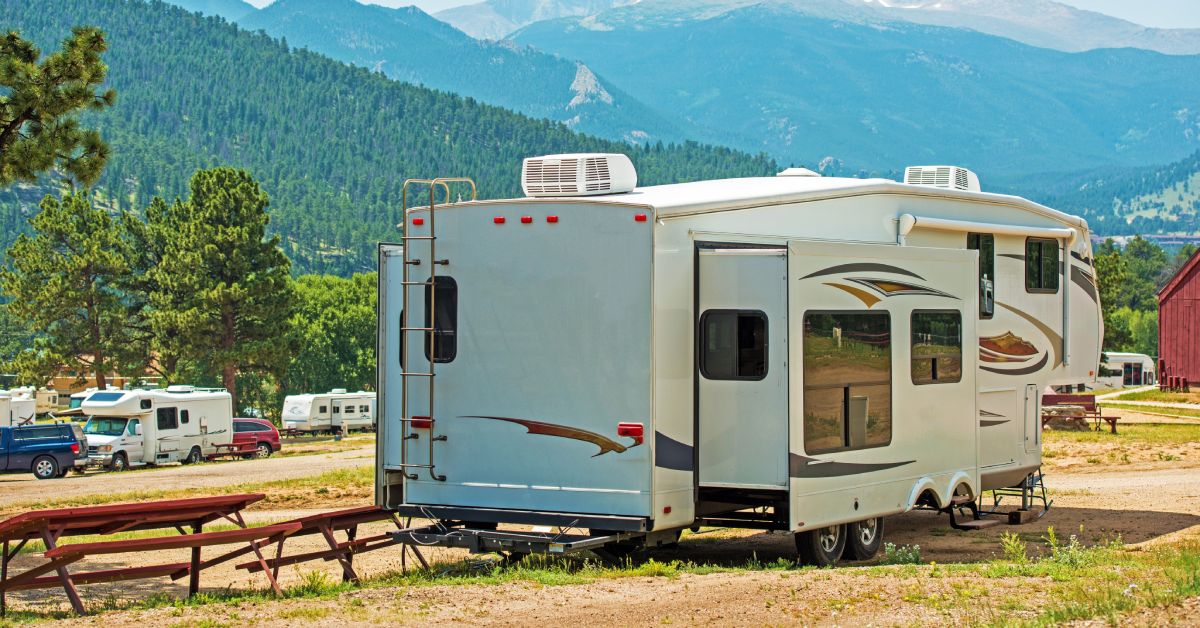 An RV parked at a camp next to some picnic tables. The RV has two air conditioners installed on the roof.