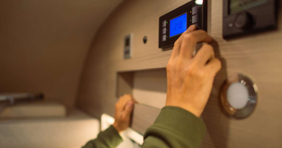 A person adjusting their RV's thermostat to cool the cabin down a bit. They reach up to a control panel to do so.