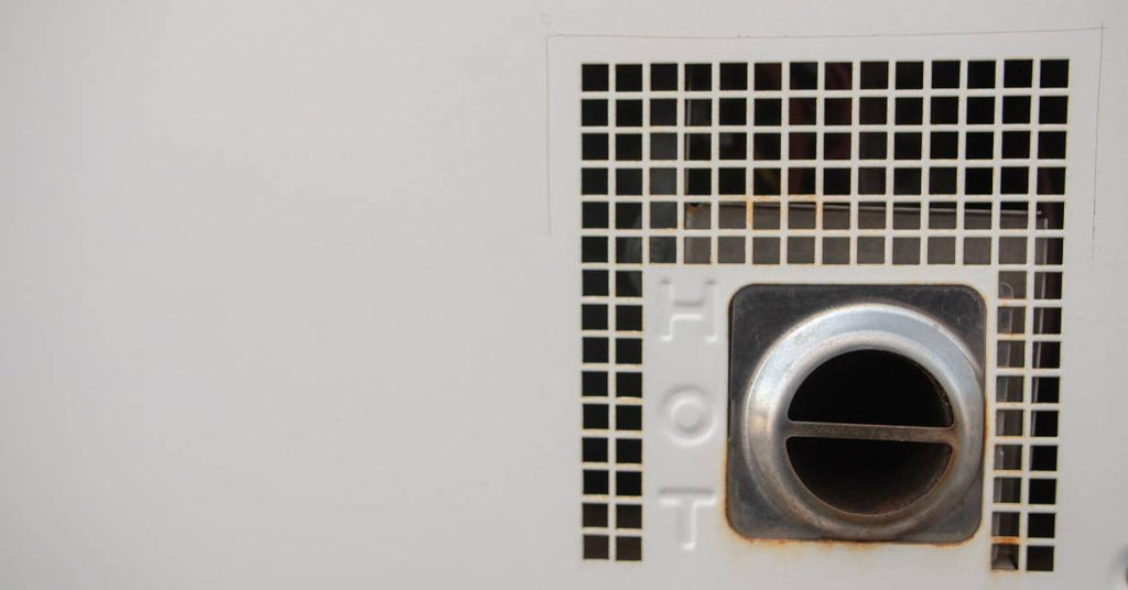 A close up of the vent of an RV water heater. The metal on the heater is white, and it's labeled as hot near the exhaust port.