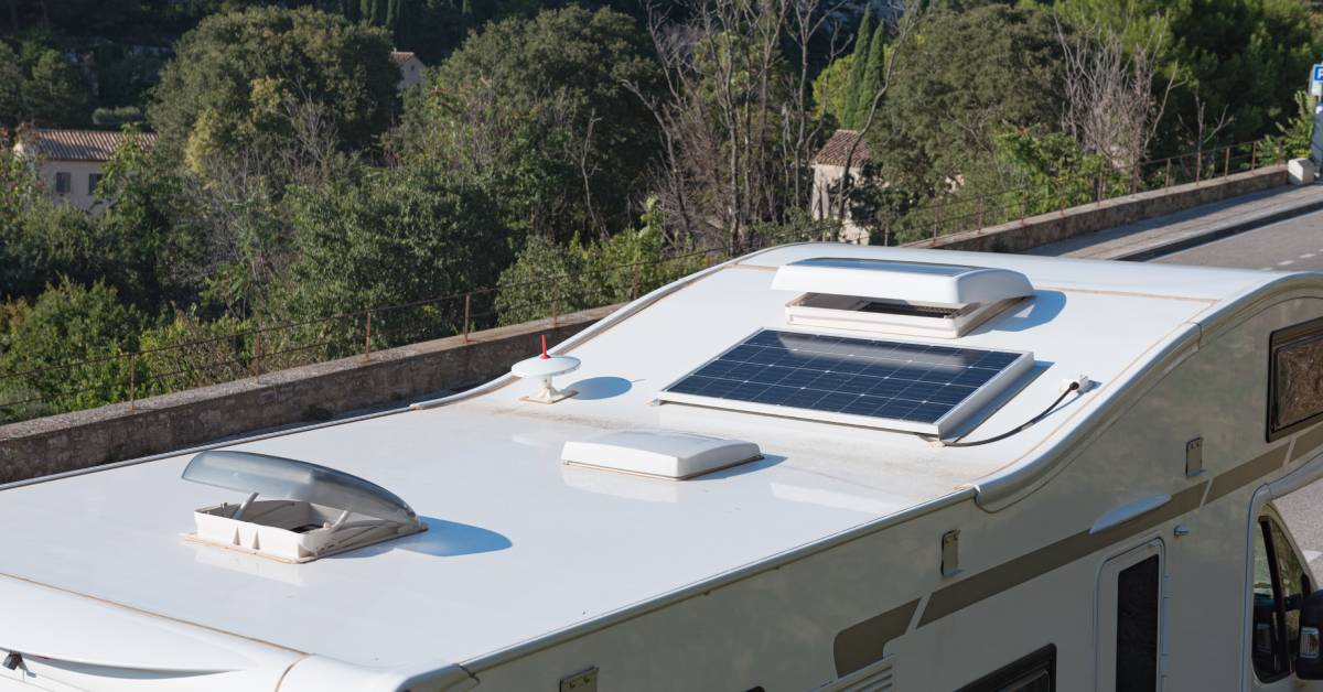 An angled view of the the roof of an RV as it drives down the road. The skylights are open, and there's a solar panel on the roof.